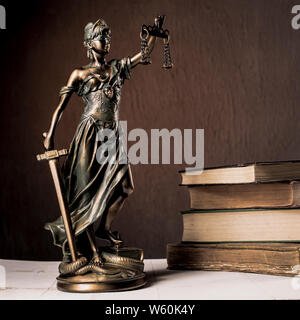 Themis figurina sorge su un bianco tavolo di legno accanto a una pila di libri antichi. Bilance legge Avvocato Concetto aziendale. - Immagine Foto Stock