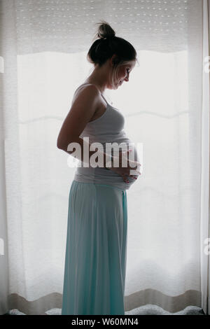 La retroilluminazione della donna incinta toccando il suo ventre Foto Stock