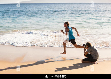 Dietro le quinte del servizio fotografico di maschio sport atleta modello funzionante per il fotografo a scattare foto per sport photoshoot. BTS sulla spiaggia. Foto Stock