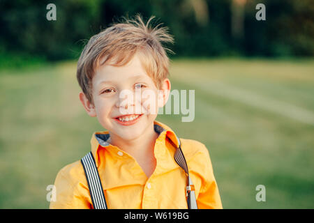 Closeup ritratto di divertente carino adorabile bella bionda sorridente bianco caucasico ragazzo di età prescolare cercando nella fotocamera contro sfondo verde chiaro outdoor presso s Foto Stock