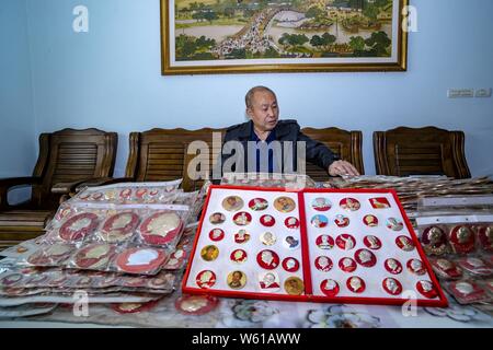 Il cinese anziano uomo Huang Junde Visualizza badge del ritratto del compianto Presidente Mao Zedong ha raccolto in questi ultimi cinquant'anni nella sua casa di Chong Foto Stock