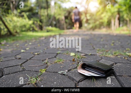 L'uomo ha perso il suo portafoglio in pelle sulla strada durante la deambulazione o la corsa nel parco con all'interno di banconote Foto Stock