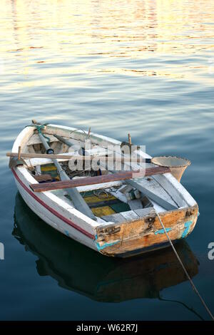 Vranjic, Croazia - 20 Luglio 2019: Piccoli vecchi weathered martoriata pittoresco a remi in legno barca da pesca riflettendo sulla calma il mare blu profondo al tramonto. Foto Stock