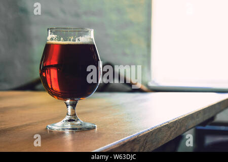 Bicchiere di birra scura sul tavolo di legno contro sfondo mattone. Il freddo deliziosa bevanda viene preparata per la festa di un amico. Concetto di bevande, divertente, riunione, Oktoberfest. Copyspace. Foto Stock