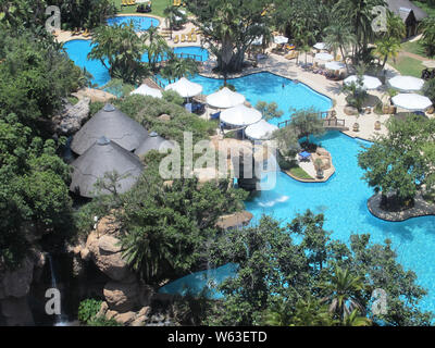 Vista aerea o guardando in giù su un hotel resort piscina circondata da alberi e ombrelloni con acqua turchese a Sun City, in Sudafrica Foto Stock