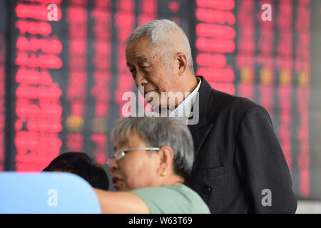 Investitori cinesi guardare i prezzi delle azioni (rosso per il prezzo in aumento e verde per la caduta dei prezzi) in corrispondenza di un magazzino casa di brokeraggio in città Fuyang, est della Cina di Foto Stock