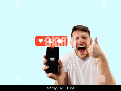 I social media le interazioni sul telefono cellulare. Internet marketing digitale, Chating, commentando e gradimento. Sorrisi e le icone sopra lo schermo dello smartphone, che azienda dal giovane uomo su blu di sfondo per studio. Foto Stock
