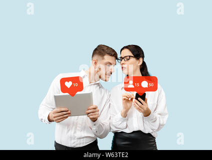 I social media le interazioni sul telefono cellulare. Internet marketing digitale, Chating, commentando e gradimento. Sorrisi e le icone sopra lo schermo tablet, che il mantenimento di una giovane coppia in blu di sfondo per studio. Foto Stock