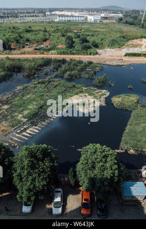 Vista aerea di acqua inquinata scaricata da un impianto di trattamento dei liquami per formare un enorme stagno di liquame in prossimità di edifici residenziali a Wuhan City, centra Foto Stock