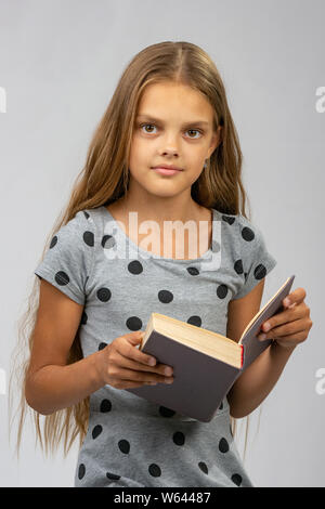 Bella ragazza di 10 anni legge un libro e si guarda nel telaio Foto Stock