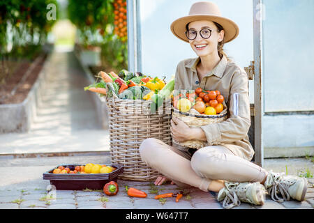 Ritratto di una giovane donna di fresco con presentate spennate vario verdure. La raccolta nella serra di una piccola azienda agricola Foto Stock