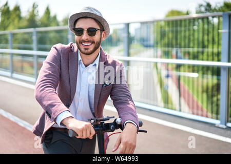 Ritratto di elegante uomo su scooter elettrico durante la giornata di sole Foto Stock