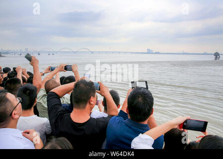 I visitatori e i residenti locali guarda le onde provenienti da una linea di alesaggio di marea del Fiume Qiantang fragoroso oltre il fiume nella città di Hangzhou, a est della Cina di Zhejian Foto Stock