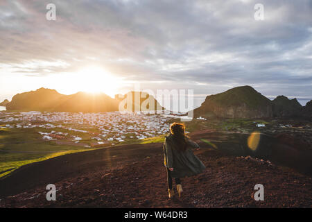 Giovane donna felice godersi il tramonto sul picco del vulcano Eldfell con vista panoramica di Vestmannaeyjar isola in Islanda. Wanderlust concetto di viaggio. Amazi Foto Stock