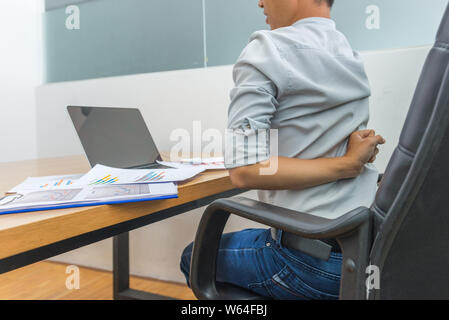 Lavoratore di ufficio avente il dolore alla schiena seduta nella parte anteriore del computer portatile Foto Stock