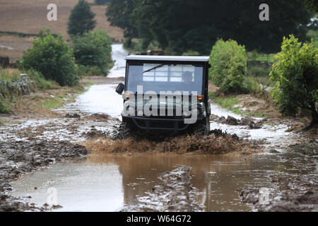 Un uomo trascina lungo una strada allagata in Grinton, North Yorkshire, dopo le parti della regione avevano fino a 82.2mm di pioggia in 24 ore il martedì. Foto Stock