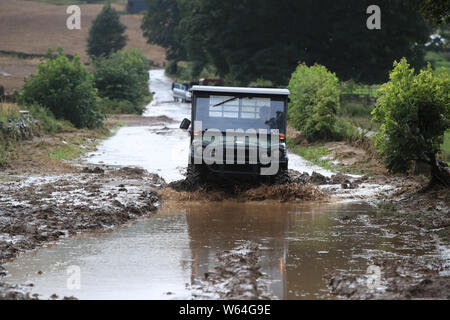 Un uomo trascina lungo una strada allagata in Grinton, North Yorkshire, dopo le parti della regione avevano fino a 82.2mm di pioggia in 24 ore il martedì. Foto Stock