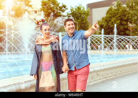 Felice coppia diversificata in amore holding hands godetevi una passeggiata serale sulla strada di città - amare uomo maturo e funky, giovane donna camminare insieme - husb sorridente Foto Stock