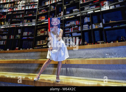 Un membro del personale di Chengdu Yan Ji Bookstore si pone per una prospettiva forzata fotografia con un libro con il ritratto della actrice americano e il modello M Foto Stock