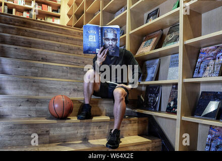 Un membro del personale di Chengdu Yan Ji Bookstore si pone per una prospettiva forzata fotografia con un libro con il ritratto del pensionato stella NBA Tim Duncan Foto Stock