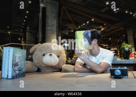 Un membro del personale di Chengdu Yan Ji Bookstore si pone per una prospettiva forzata fotografia con la copertina del libro di 'Le voleur d'ombres" con lo scrittore francese Foto Stock