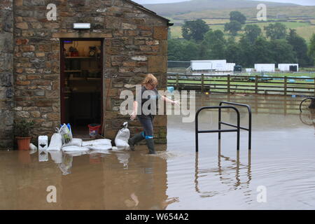 Una donna cammina attraverso l'acqua di allagamento al di fuori Dales Cafe e Cakery nello Yorkshire, dopo le parti della regione avevano fino a 82.2mm di pioggia in 24 ore il martedì. Foto Stock