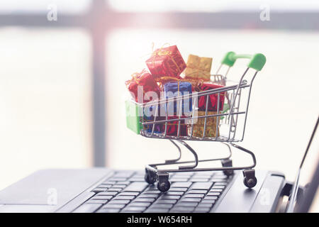 Carrello spesa, piccole scatole e laptop. Shopping online concetto. Foto Stock