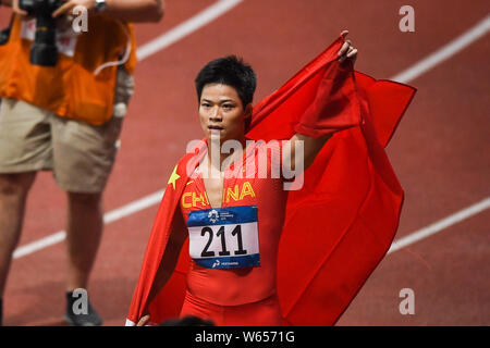 Su Bingtian della Cina pone con la bandiera nazionale cinese per festeggiare dopo la conquista degli uomini 100m finale delle gare di atletica durante il 2018 Asi Foto Stock