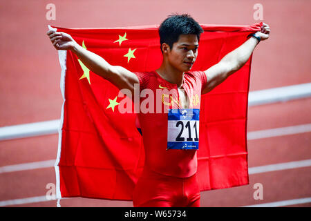 Su Bingtian della Cina pone con la bandiera nazionale cinese per festeggiare dopo la conquista degli uomini 100m finale delle gare di atletica durante il 2018 Asi Foto Stock