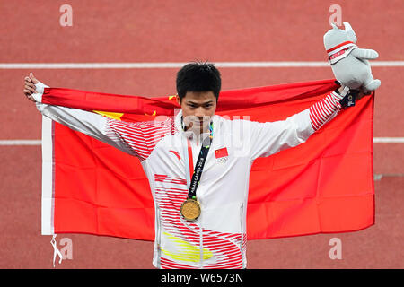 Su Bingtian della Cina pone con la bandiera nazionale cinese per festeggiare dopo la conquista degli uomini 100m finale delle gare di atletica durante il 2018 Asi Foto Stock