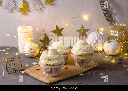 Crema bianca tortine come una vacanza di Natale decorazione con stelle dorate topper tra l Anno nuovo décor, candele e luci Foto Stock