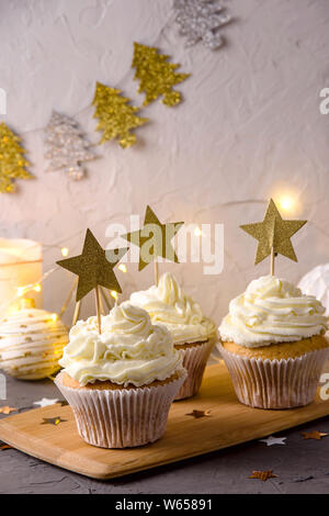 Crema bianca tortine come una vacanza di Natale decorazione con stelle dorate topper tra l Anno nuovo décor, candele e luci Foto Stock