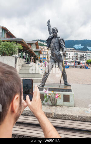 Giovane uomo prendendo la foto del famoso Freddie Mercury statua sulla piazza del mercato di fronte al Lago di Ginevra (Lac Leman) in Montreux, Vaud, Svizzera Foto Stock