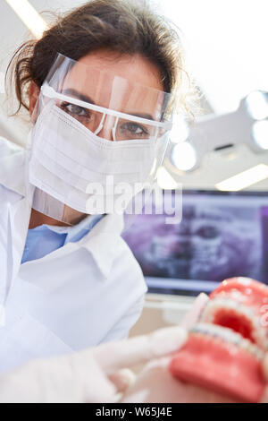 La donna come un dentista o chirurgo orale con mascherina chirurgica e visiera di punti a un modello di protesi Foto Stock