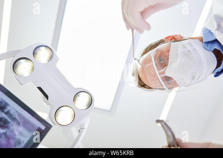 Chirurgo orale con visiera e mascherina chirurgica durante un funzionamento di emergenza in una clinica dentale Foto Stock