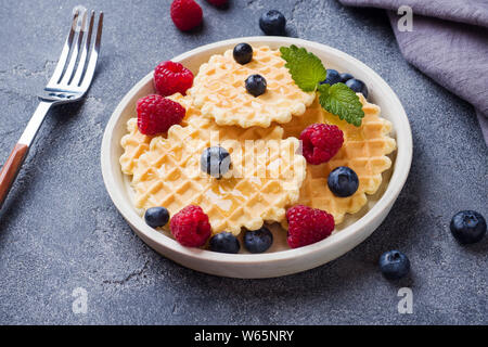 Waffle ondulato i cookie con lamponi freschi e mirtilli al buio su un sfondo di calcestruzzo. Spazio di copia Foto Stock