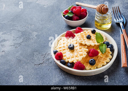 Waffle ondulato i cookie con lamponi freschi e mirtilli al buio su un sfondo di calcestruzzo. Spazio di copia Foto Stock