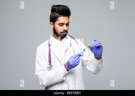 Focalizzato medico indiano maschio guardando la siringa con la medicina isolato su bianco di sfondo per studio Foto Stock
