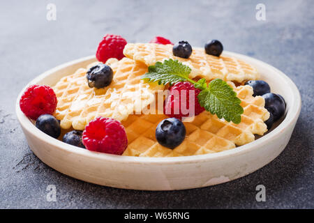 Waffle ondulato i cookie con lamponi freschi e mirtilli al buio su un sfondo di calcestruzzo. Spazio di copia Foto Stock