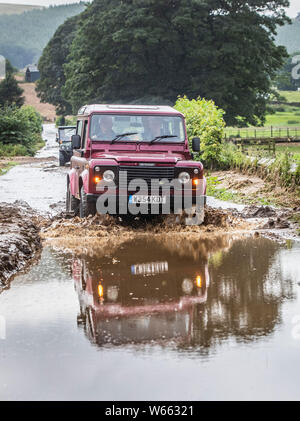 Un uomo trascina lungo una strada allagata vicino Grinton, North Yorkshire, dopo le parti della regione avevano fino a 82.2mm di pioggia in 24 ore il martedì. Foto Stock