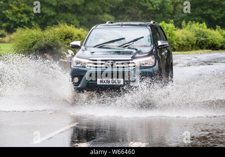 Un uomo trascina lungo una strada allagata vicino Grinton, North Yorkshire, dopo le parti della regione avevano fino a 82.2mm di pioggia in 24 ore il martedì. Foto Stock