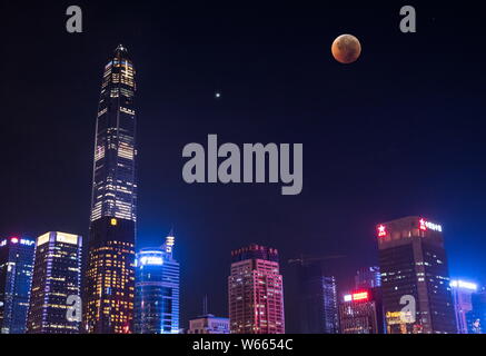 Vista la più lunga "sangue luna' eclissi di questo secolo, a destra che passa nel cono d'ombra della Terra e Marte nel cielo sopra i grattacieli durante Foto Stock