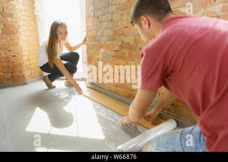 Coppia giovane facendo appartamento riparare insieme se stessi. Uomo sposato e la donna facendo home makeover o rinnovo. Concetto di relazioni, la famiglia, l'amore. Di cui pavimenti in laminato, sorridono felici. Foto Stock