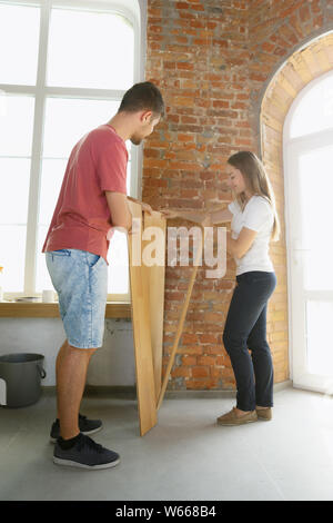 Coppia giovane facendo appartamento riparare insieme se stessi. Uomo sposato e la donna facendo home makeover o rinnovo. Concetto di relazioni, la famiglia, l'amore. Di cui pavimenti in laminato, sorridono felici. Foto Stock