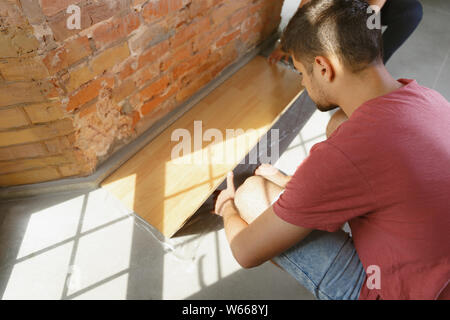 Coppia giovane facendo appartamento riparare insieme se stessi. Uomo sposato e la donna facendo home makeover o rinnovo. Concetto di relazioni, la famiglia, l'amore. Di cui pavimenti in laminato, sorridono felici. Foto Stock