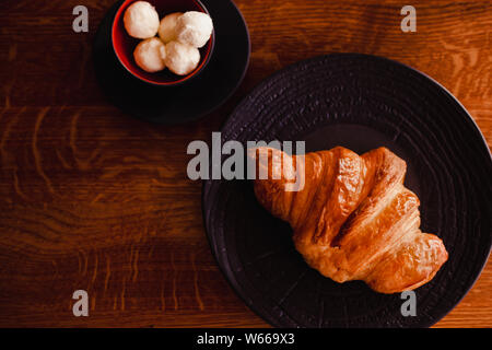 Croissant cotta su una piastra nera con tazza di burro sullo sfondo di legno. Panificio Breacfast ristorante stile di vita. Foto Stock