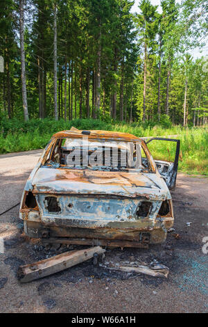 Bruciato auto presso una strada nel bosco Foto Stock