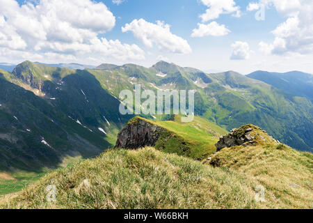 Lo splendido paesaggio di montagna Fagaras. rocce su ripidi pendii erbosi. neve nella profonda valle. splendida estate meteo con le nubi del cielo Foto Stock