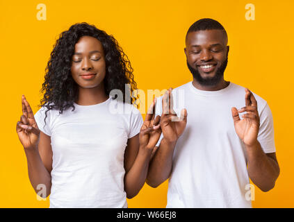 Afro giovane chiudendo gli occhi e dita incrociate con la speranza Foto Stock