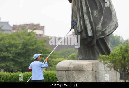Un lavoratore cinese pulisce una statua in bronzo di cinesi monaco buddista Xuanzang girando in verde nella parte anteriore del gigante della Pagoda dell'Oca Selvaggia o Big Wild Goose Pago Foto Stock